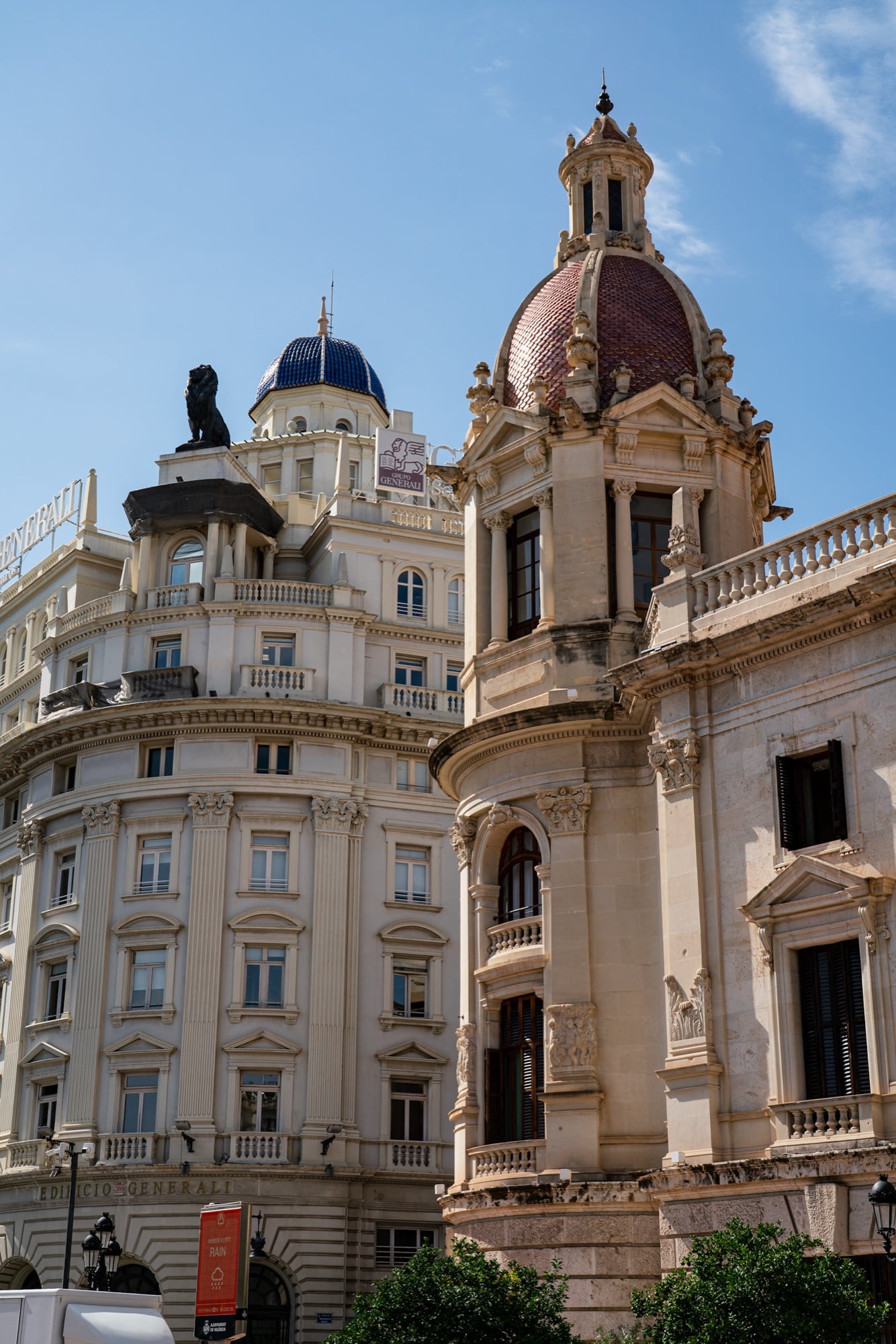 A blue-tiled dome and a red-tiled cupola crowning neighbouring corner buildings against a deep blue sky