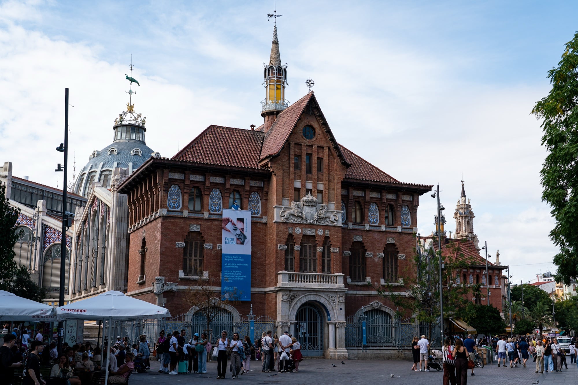 A red-brick building with a spired turret beside the domes of the Mercado Central, crowds filling the square