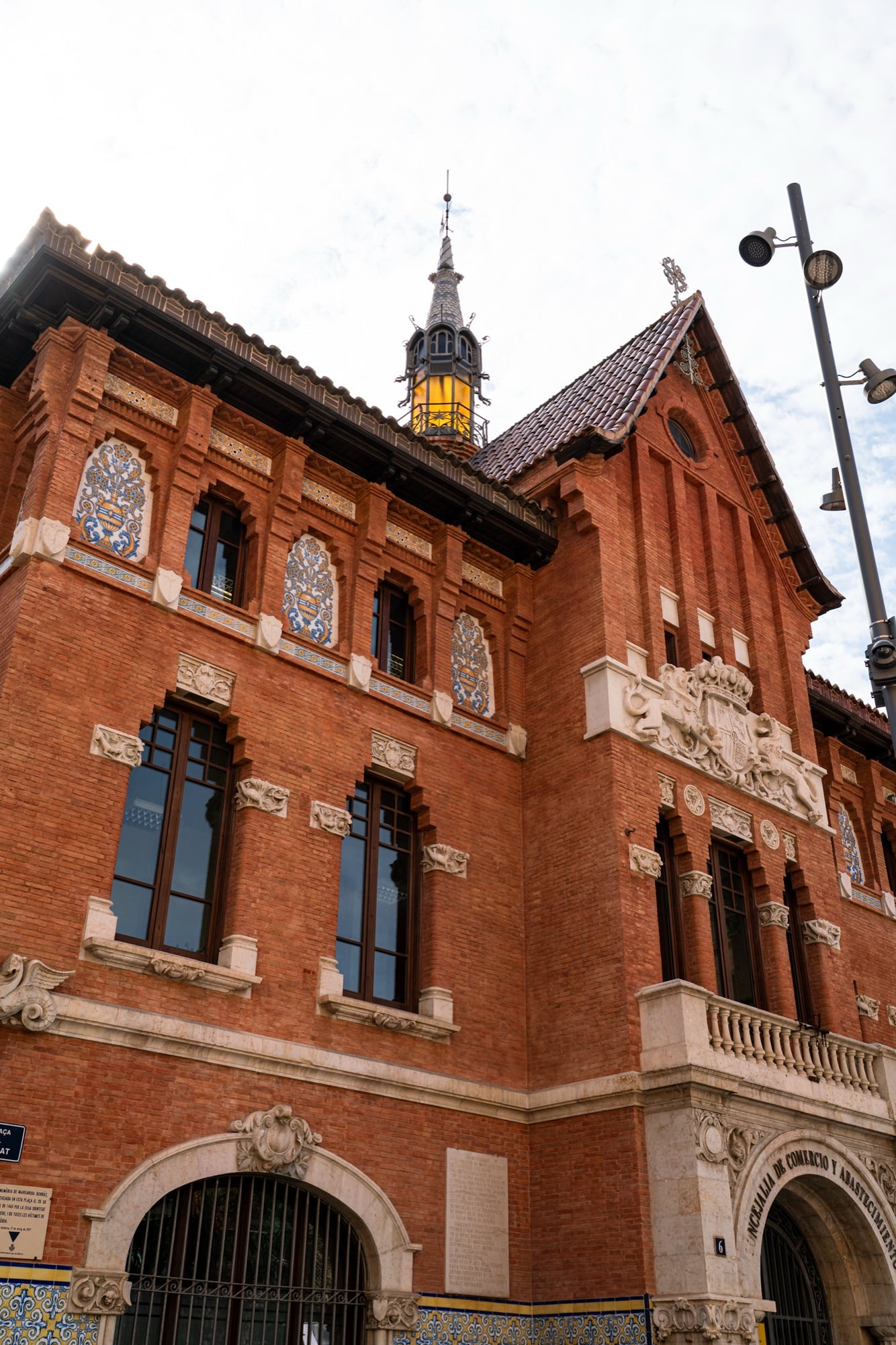 Looking up at a red-brick building with tiled roundels, carved stonework and a slender spired turret