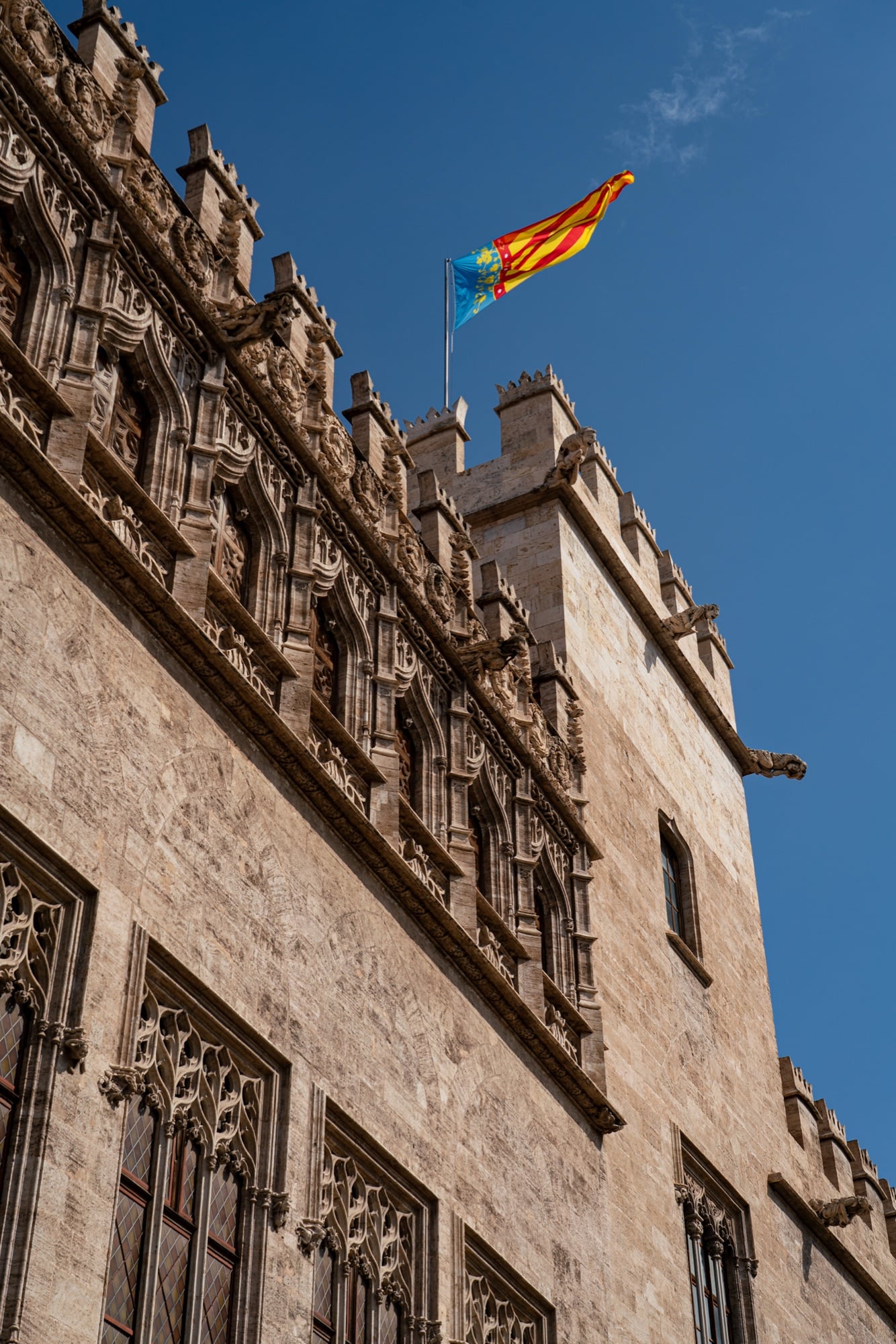 The carved Gothic windows and crenellated battlements of La Lonja de la Seda, the Valencian flag flying above